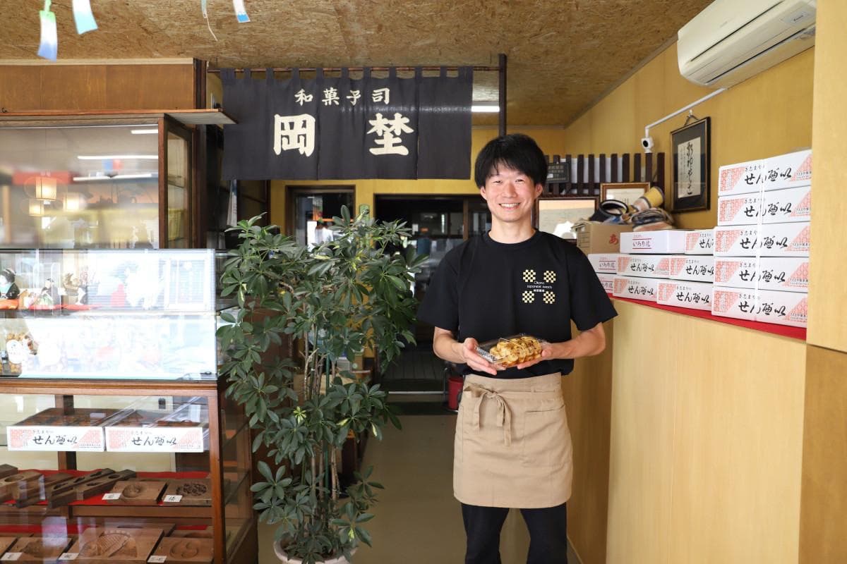 A staff member holding the large mitarashi dango inside Okano Seikaten